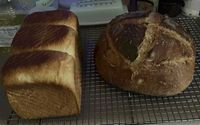 A three segment milk bread and circular rustic french loaf on a cooling rack.