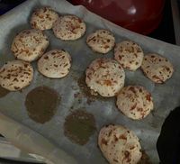 A batch of circular tapioca flour cheese bread with a crispy crust on a paper-lined baking pan.